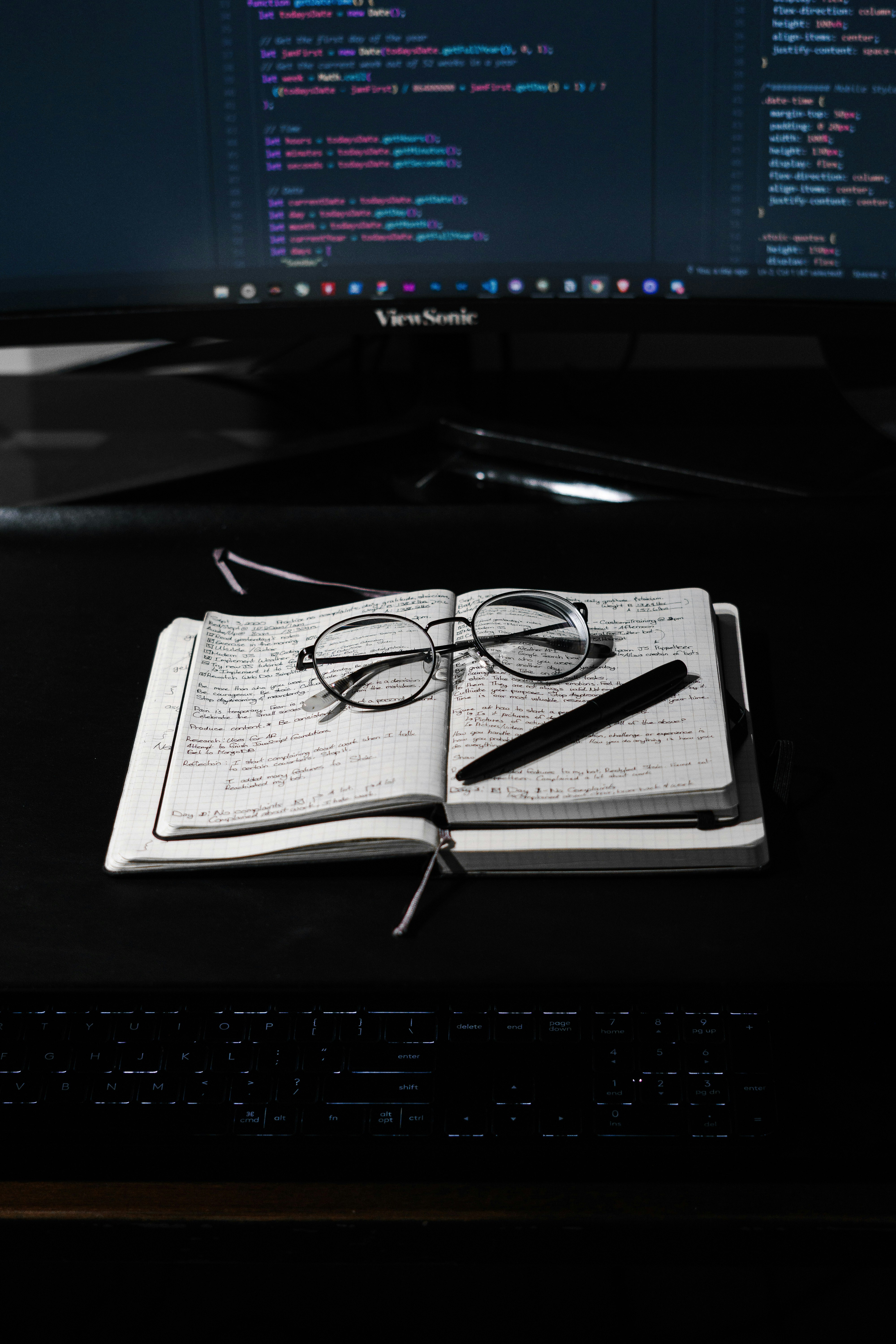 A pair of glasses, pen and two open notebooks in black and white